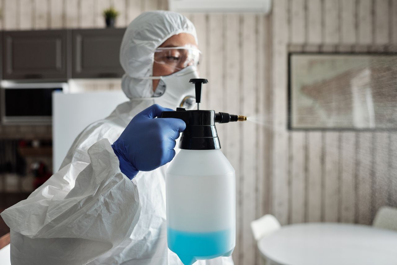 services-04 Professional in full gear disinfecting indoor area using a spray bottle for COVID-19 prevention.